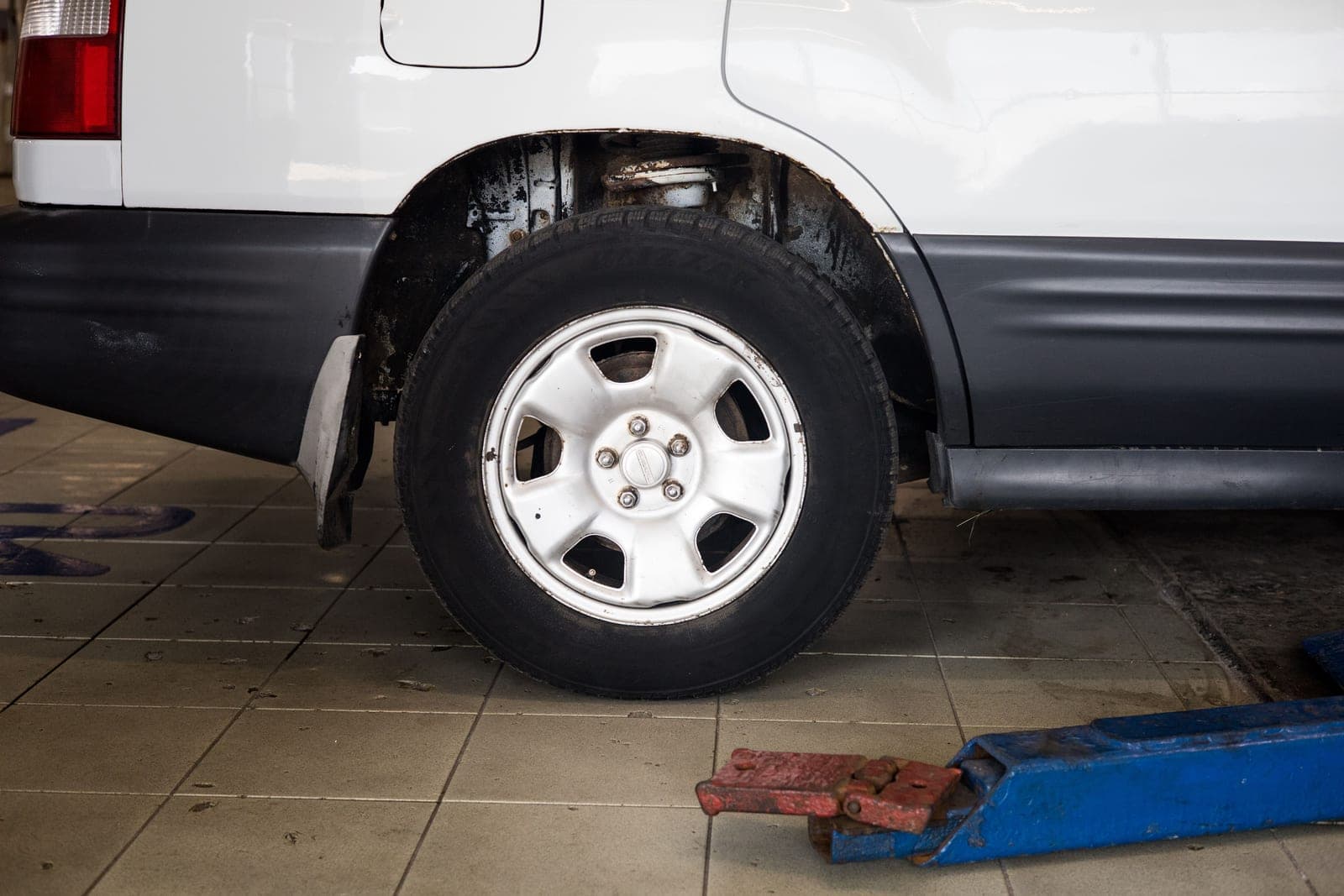 A car wheel in an auto repair shop with a hydraulic jack in place
