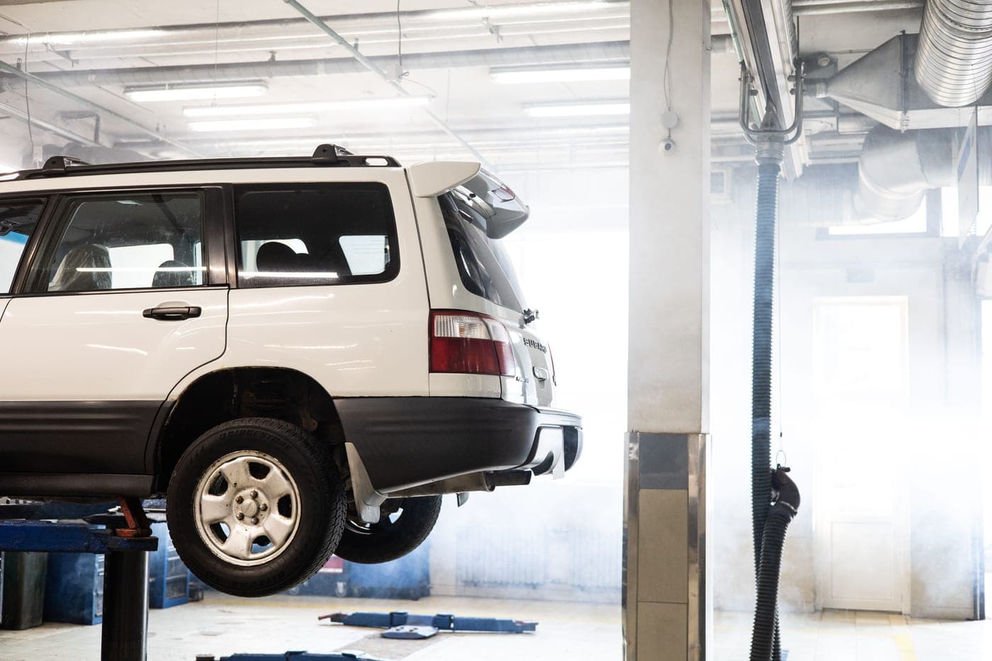 A white SUV elevated on a lift inside an auto repair shop for maintenance